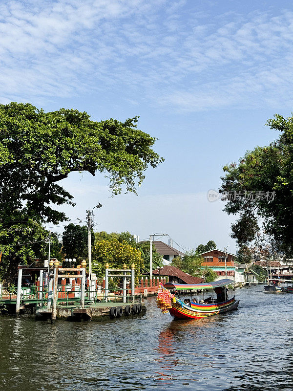 一艘带顶篷的木船载着游客在Khlong Damnoen Saduak运河附近游览，游船行驶在通往Tha Chin和Mae Klong河的水路上